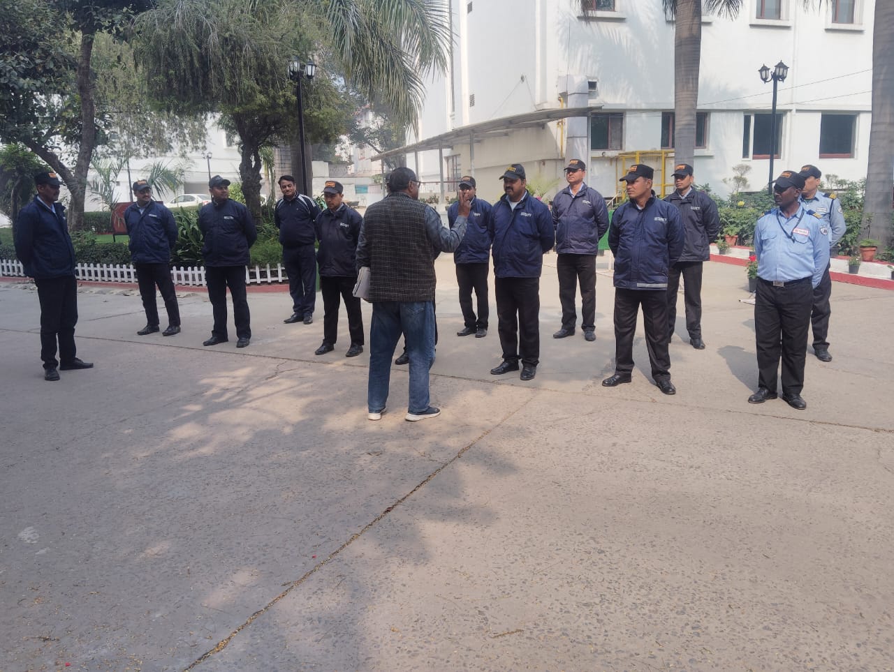 An instructor in civilian clothes briefing a semi-circle of security guards outdoors